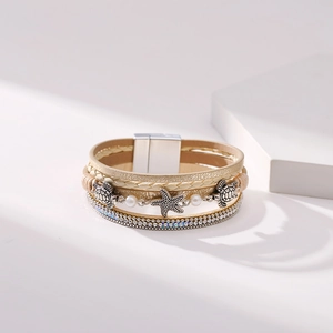 Detail of bohemian layered bracelet with starfish and turtle charms on white display blocks