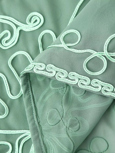 Détail des broderies décoratives et du tissu tissé sur l'ensemble robe vert clair