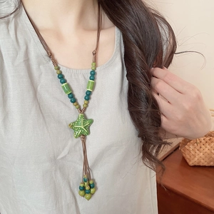 Detail view of a green ceramic starfish pendant necklace worn by a model in boho style