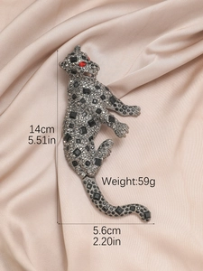 Macro shot of gun-grey leopard brooch with red crystals on beige silk fabric