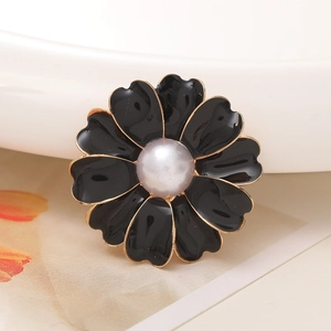 Detail of a black enamel flower charm with gold edging and a pearl center on a floral card