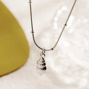 Silver conch shell pendant necklace with beaded snake chain on a soft warm background