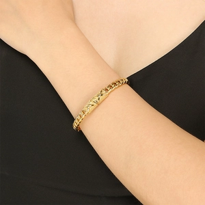Detailed view of wide gold wave twisted metal bracelet worn on a woman's wrist