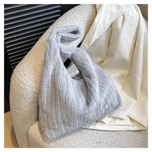 Close-up of grey plush tote bag on beige textured sofa with white blazer detail