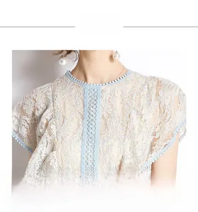 Close-up of light blue lace top featuring intricate crochet and pom-pom trim round neck