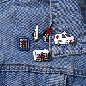 Five medical enamel pins with rhinestones featuring an ambulance and first aid kit on denim