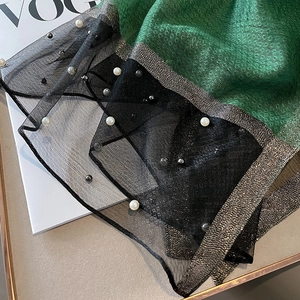 Close-up of black mesh scarf featuring white pearls and golden metallic woven edges
