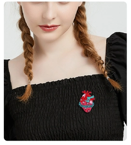 Detailed close-up of a red heart brooch with blue vines pinned on a black top