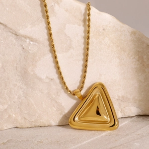 Detailansicht einer goldenen Kordelkette mit massivem Dreiecksanhänger auf hellem Stein