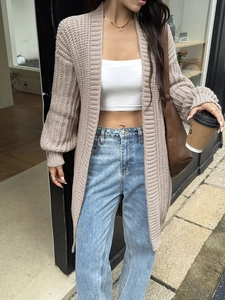 Dettaglio del lungo cardigan beige in maglia abbinato a crop top bianco e jeans in denim