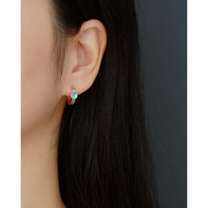 Close-up of model wearing small silver huggie hoop earring with light blue opal stone