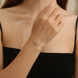 Detail of a gold titanium bracelet with a diamond square pendant on a woman wrist