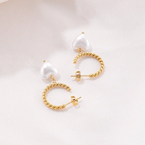 Créoles dorées torsadées avec pendentifs en perles en forme de cœur sur fond de soie rose