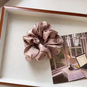 Detail view of pink satin scrunchie with silky luster in a minimalist wooden tray