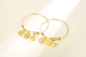 Detail of woven gold-plated titanium steel constellation bangles with zodiac charms