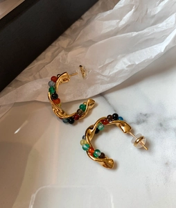 Detailed shot of gold C-shaped hoop earrings with colorful beads on marble