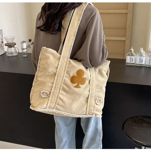 Detail of beige corduroy tote bag with fringe edges and brown clover patch on a shoulder