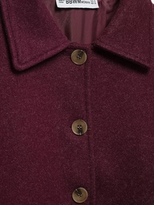 Detailed close-up of burgundy wool-like texture with tortoiseshell buttons and lapel