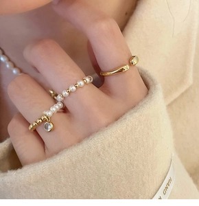 Détail macro de bagues superposées en plaqué or avec perles et zircons sur main