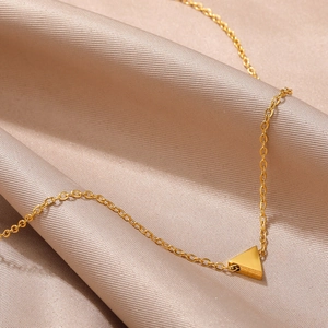 Close-up of golden O-chain necklace with minimalist triangular pendant on silk