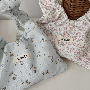 Detailed macro view of floral cotton wrist bags with gathered handles and brand labels