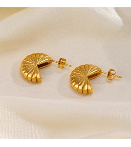 Macro view of C-shaped gold-plated earrings with shell-like textures on silk background