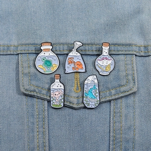 Five ocean creature enamel pins in glass bottles pinned on a blue denim jacket pocket