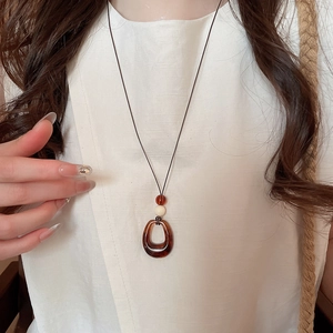 Gros plan du collier pendentif en résine ambrée avec perle blanche sur coton doux