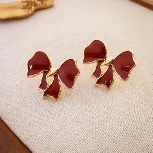 Vintage dark red bow earrings with gold heart detail on a beige textured background