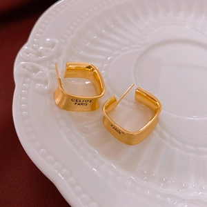 Detail view of gold-plated square hoop earrings with engraved Paris lettering on red fabric