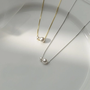 Close-up of gold and silver wheat ear pearl necklaces on a minimalist ceramic plate