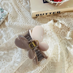 Détail d'une pince à cheveux papillon aux tons morandi sur fond de dentelle blanche