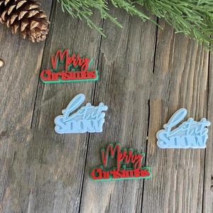 Flat lay of Merry Christmas and Let it Snow acrylic cake toppers on wood background