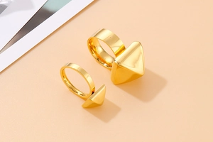 Detailed view of two polished gold geometric triangle rings on a warm beige background