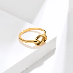 Macro detail of golden knotted titanium steel ring on a white minimalist pedestal
