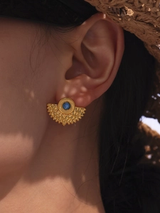 Detail of turquoise fan-shaped gold stud earring worn by model in a boho resort setting