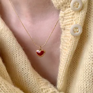 Golden titanium steel chain necklace with red heart pendant worn on a knit cardigan