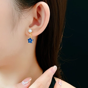 Close-up of elegant gold clover earring with blue enamel and white pearl on model