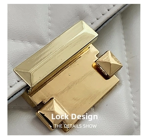 Detailed macro view of the gold metal lock and quilted leather pattern on the white bag