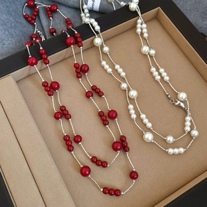 Detail view of long layered necklace with red and white pearls on brown velvet tray