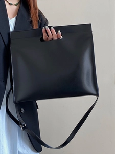 Close-up of black leather business tote bag with unique cut-out handle and adjustable strap