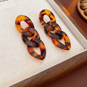 Dettaglio di orecchini vintage con catena leopardata in resina ambrata su legno