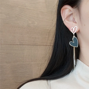 Detail showing asymmetrical silver heart earrings with long fringe chains on a model