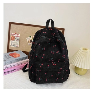 Close-up of black corduroy backpack with red cherry patterns on a white table