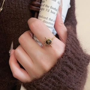 Detail of sunburst gold ring with round tiger eye stone worn over a brown sweater