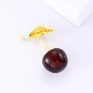 Élégante broche cerise avec fruits rouges translucides et feuilles dorées sur fond blanc