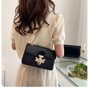 Close-up of black snakeskin embossed crossbody bag with golden bee rhinestone buckle