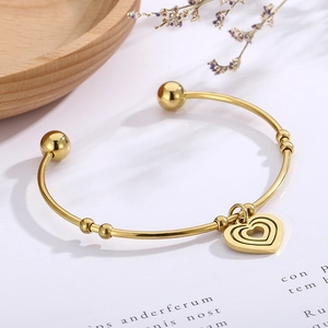 Detail of gold open heart bangle showing polished finish and charms on a wooden tray