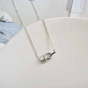 Detail shot of silver titanium knot pendant necklace on white minimalist background