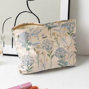 Dettaglio della trousse jacquard beige con motivi di ortensie blu e cerniera in metallo